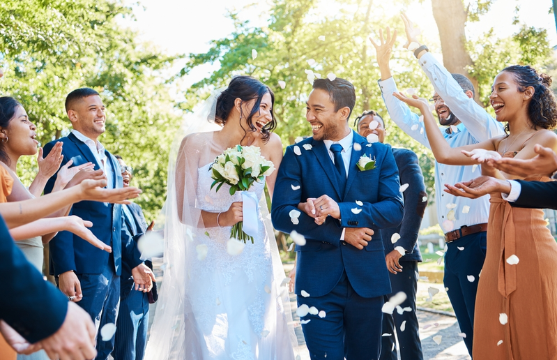 newly married bride and groom with guests throwing white flower petals