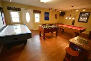 A cabin game room with an air hockey table, pool table, arcade, and foosball table in a yellow room